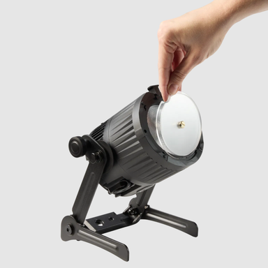Astera QuikBeam rotatable elliptical filter being installed by hand onto QuikBeam light fixture with barndoor attached grey background