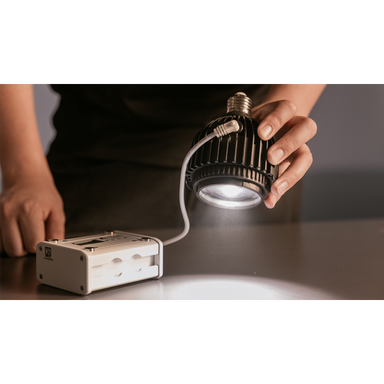 Astera SolaBulb in use hand holding bulb emitting warm white light beam onto surface connected to Astera PowerStation controller lifestyle shot