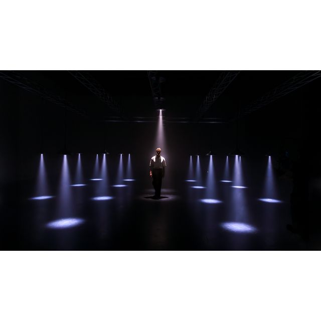 Astera SolaBulb stage lighting demonstration person standing center stage surrounded by multiple SolaBulb light beams in grid pattern on dark stage promotional shot